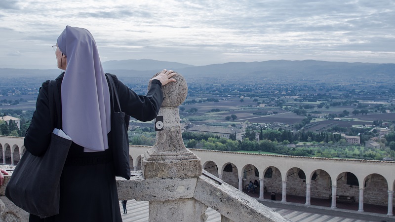 En nunna kl�dd i lila huvudduk blickar ut �ver landskapet nedanf�r Assisi.